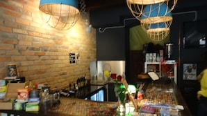 A bar area with a brick wall, blue hanging lamps, and various bottles and boxes on the counter. - Rosemary's B&B (Poznan)