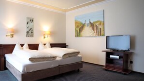 A hotel room with a double bed, two wall-mounted lamps, a painting of a beach pathway, a television on a wooden stand, and a carpeted floor. - Hotel Soldwisch (Lübeck)