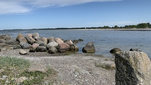 A rocky shoreline with a calm sea, a distant beach, and a clear sky. - Hotel Soldwisch (Lübeck)