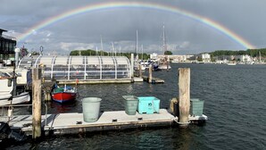 A marina with boats docked, a glass greenhouse structure, and a rainbow in the background. - Hotel Soldwisch (Lübeck)