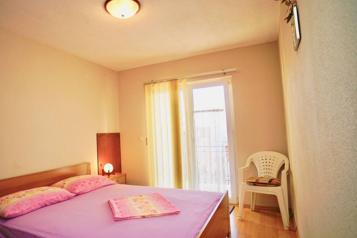 A bedroom with a bed, a nightstand, a chair, and a window with curtains.