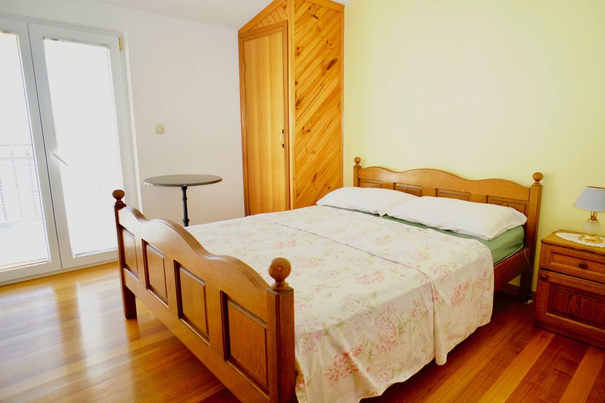 A bedroom with a wooden bed, a bedside table with a lamp, and a small round table.
