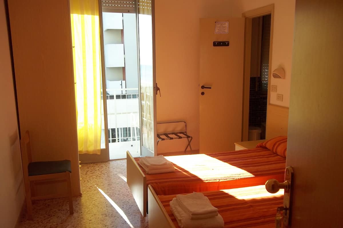 A hotel room with two beds, a chair, a small table, and a door with a sign.