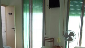 Una habitación de hotel con dos camas, una silla, un escritorio con lámpara, un televisor y un ventilador de pie.