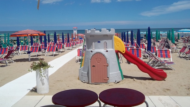 Una playa con hileras de sillas y sombrillas, una estructura de juegos para niños y una torre de salvavidas.