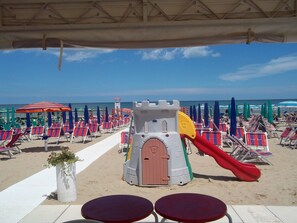 Een strand met rijen strandstoelen en parasols, een speelconstructie voor kinderen en een uitkijktoren voor de badmeester.