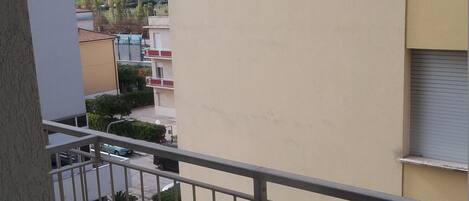 Un balcón con una mesa blanca y barandilla de metal, con vistas a una zona residencial con casas y vegetación.
