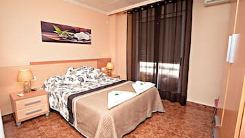 A hotel room with a bed, nightstands, a lamp, a painting, and a window with curtains.