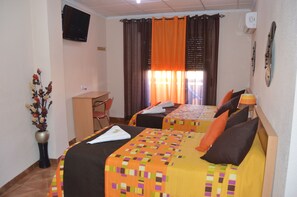 A hotel room with two beds, a desk, a chair, a TV, and a vase with flowers. - Hostal Carrizo (Elda)