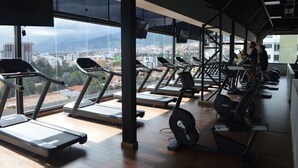 Un gimnasio con cintas de correr, bicicletas estáticas y un amplio ventanal con vista a la ciudad.