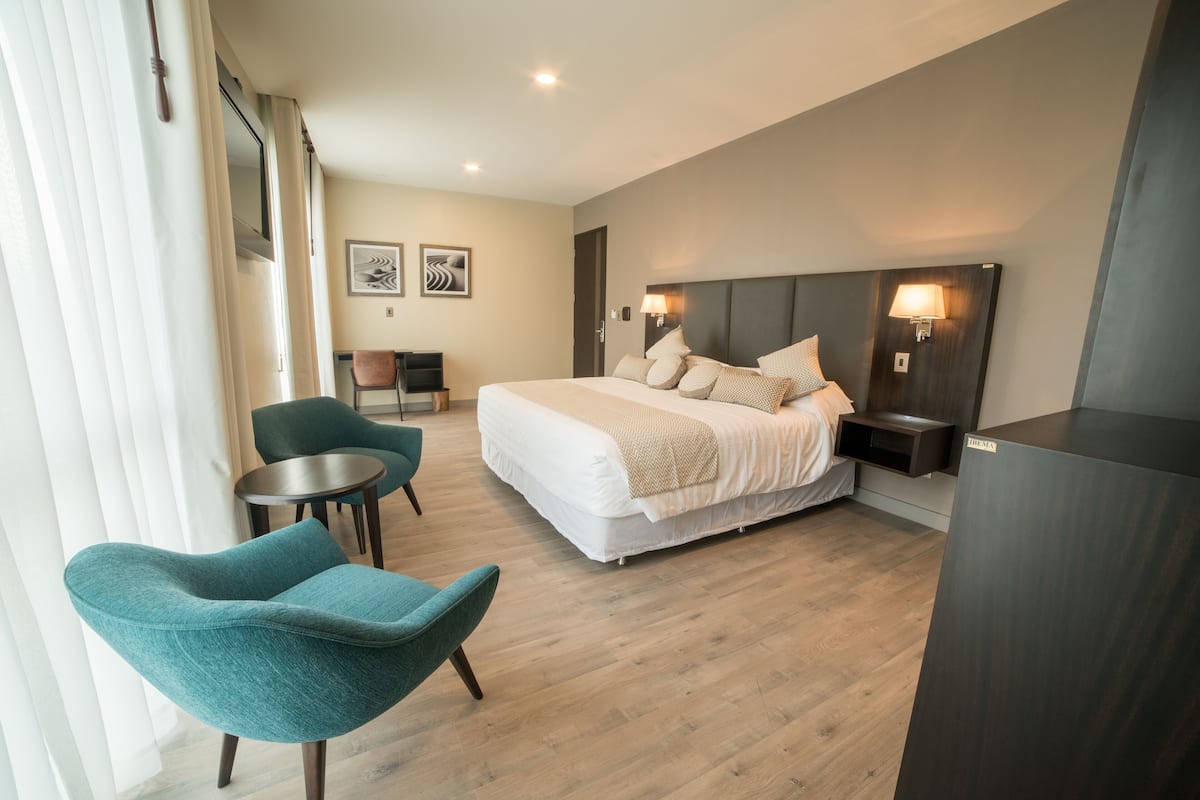 A modern hotel room with a large bed, two chairs, a small table, and a desk.