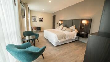 Une chambre d’hôtel moderne avec un grand lit, deux fauteuils, une petite table et un bureau.