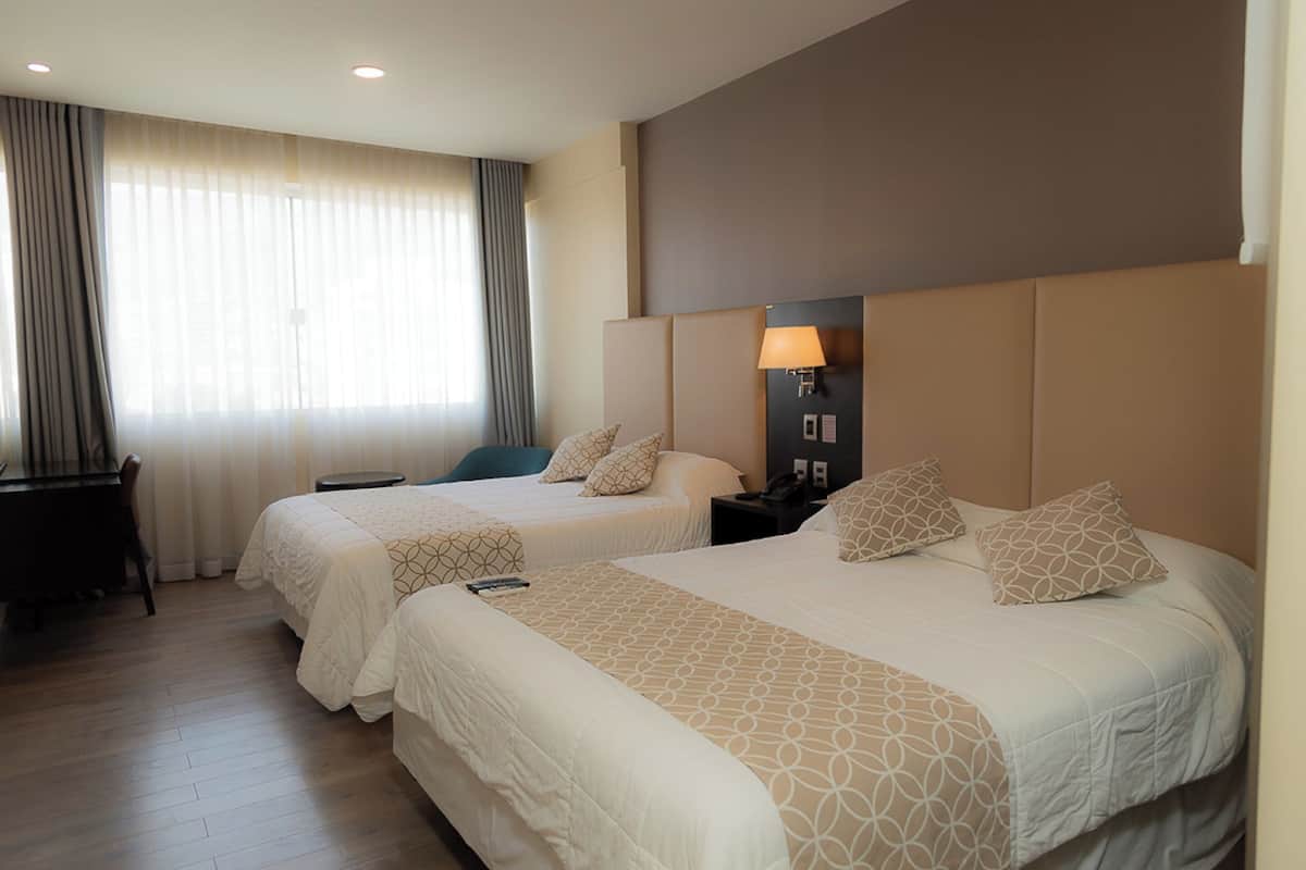 A hotel room with two beds, a desk, and a nightstand with a lamp.