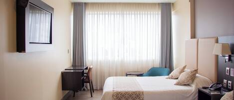 Habitación de hotel con dos camas, un escritorio, una silla y un televisor instalado en la pared.