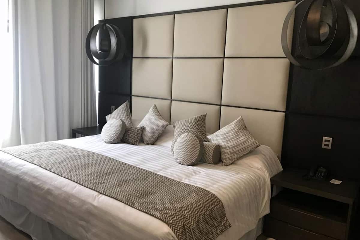 A modern hotel room with a large bed, a headboard with a geometric pattern, and a bedside table with a phone and a small lamp.
