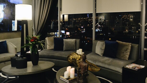 Una sala moderna con un sofá, dos mesas redondas y vistas a un paisaje urbano nocturno.