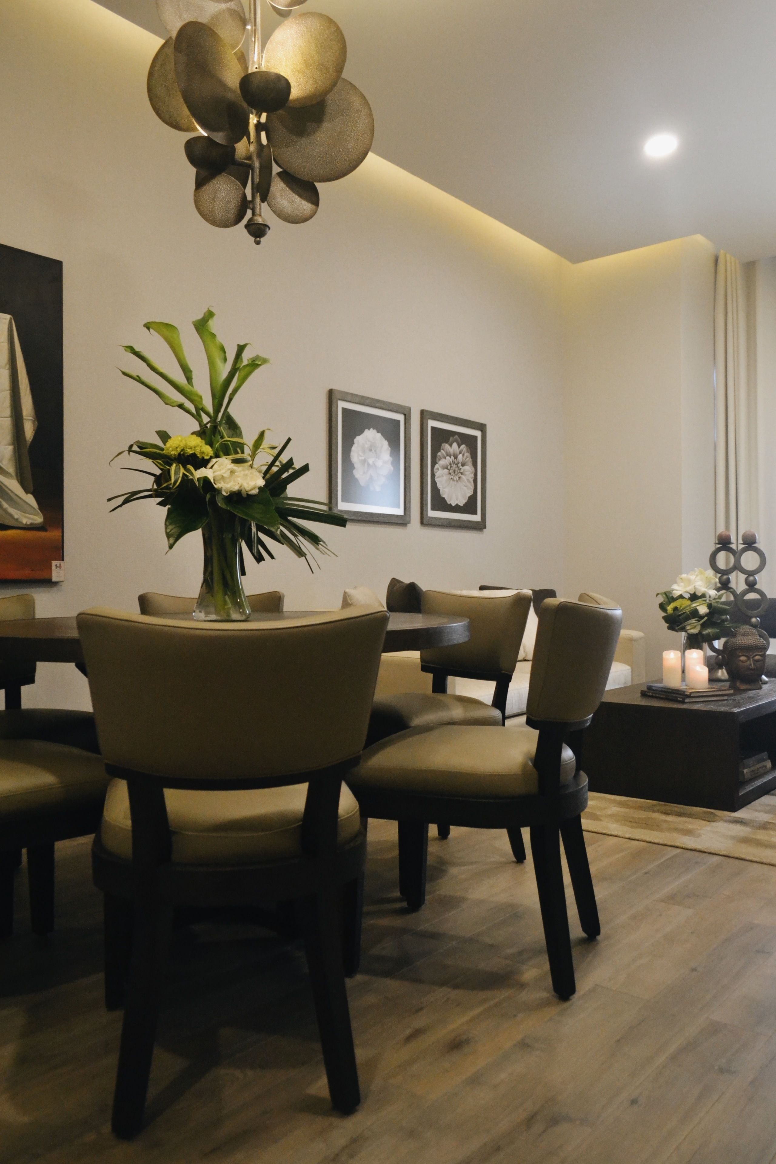 A dining area with a round table, chairs, a vase with flowers, and framed artwork on the wall.