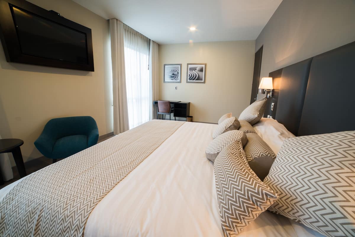 A hotel room with a large bed, a desk, a chair, and a TV on the wall.