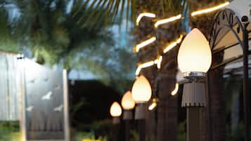 Mobiliario exterior con sillas de metal y una jardinera, bajo un farol.