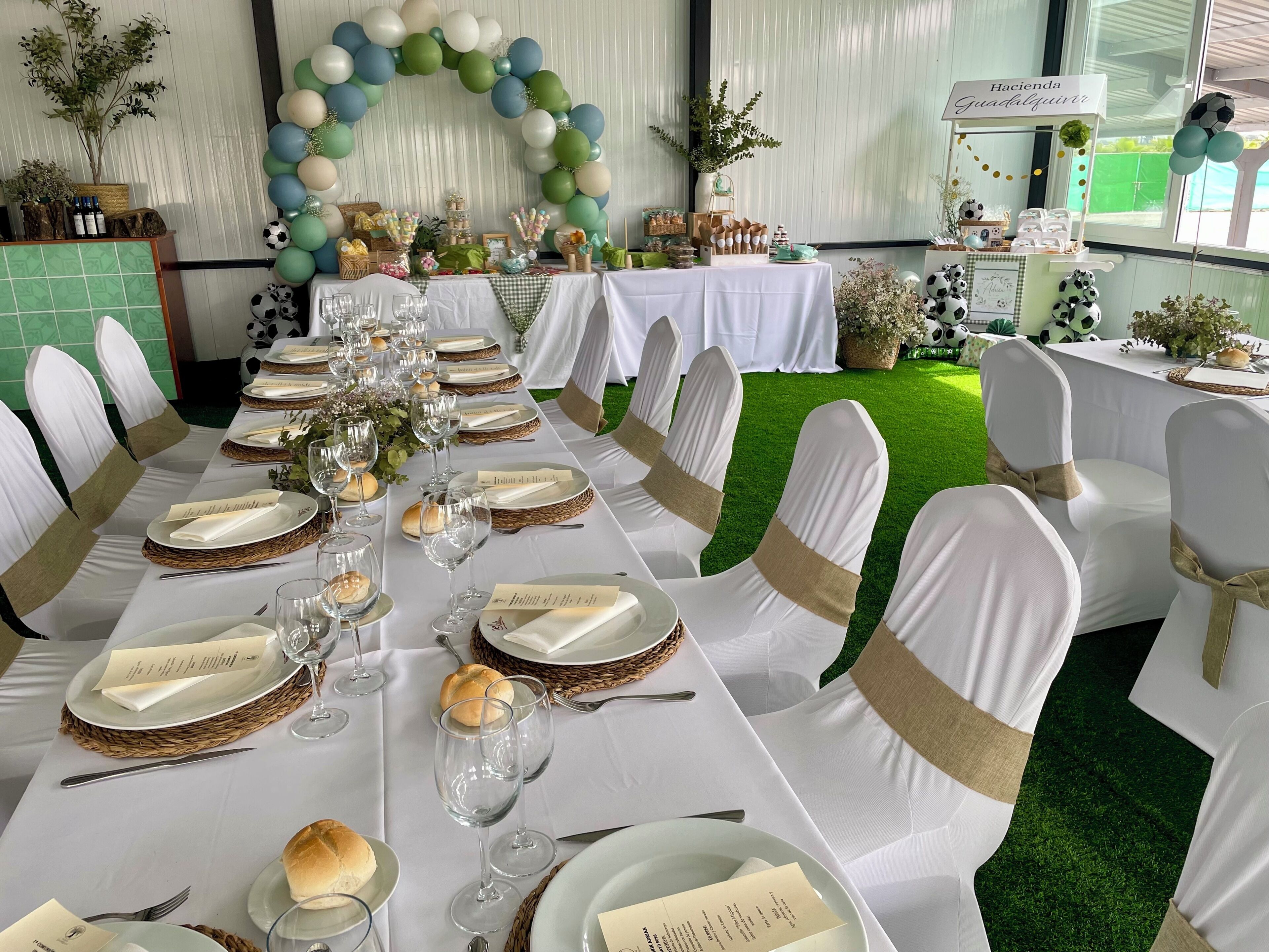 A long banquet table set for a formal event with white tablecloths, gold sashes, and clear glassware.