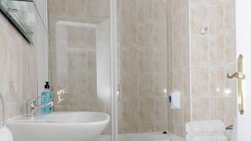 Baño con ducha compartimentada con vidrio, lavamanos pedestal, inodoro y perchero para toallas.