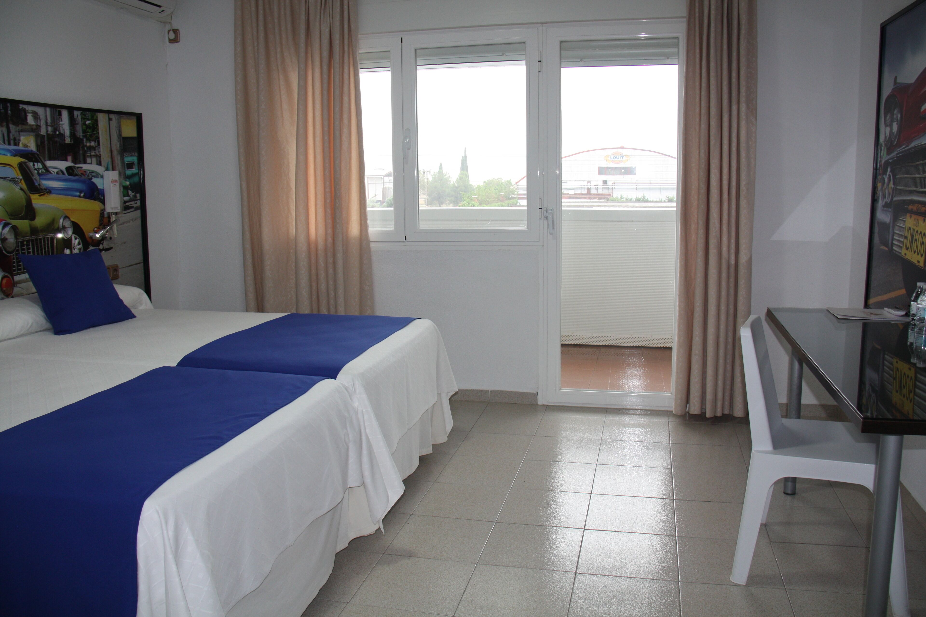 Habitación de hotel con dos camas, un escritorio y vistas al exterior.