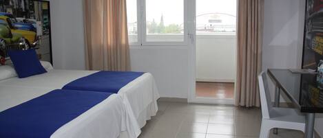 Habitación de hotel con dos camas, un escritorio y vistas al exterior.