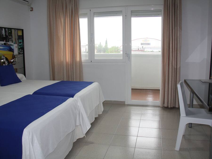 Habitación de hotel con dos camas, un escritorio y vistas al exterior.