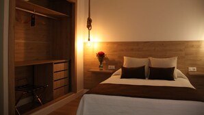 Un dormitorio con cabecera de madera, una mesita de noche con lámpara, una cama con dos almohadas y un atril con un florero.