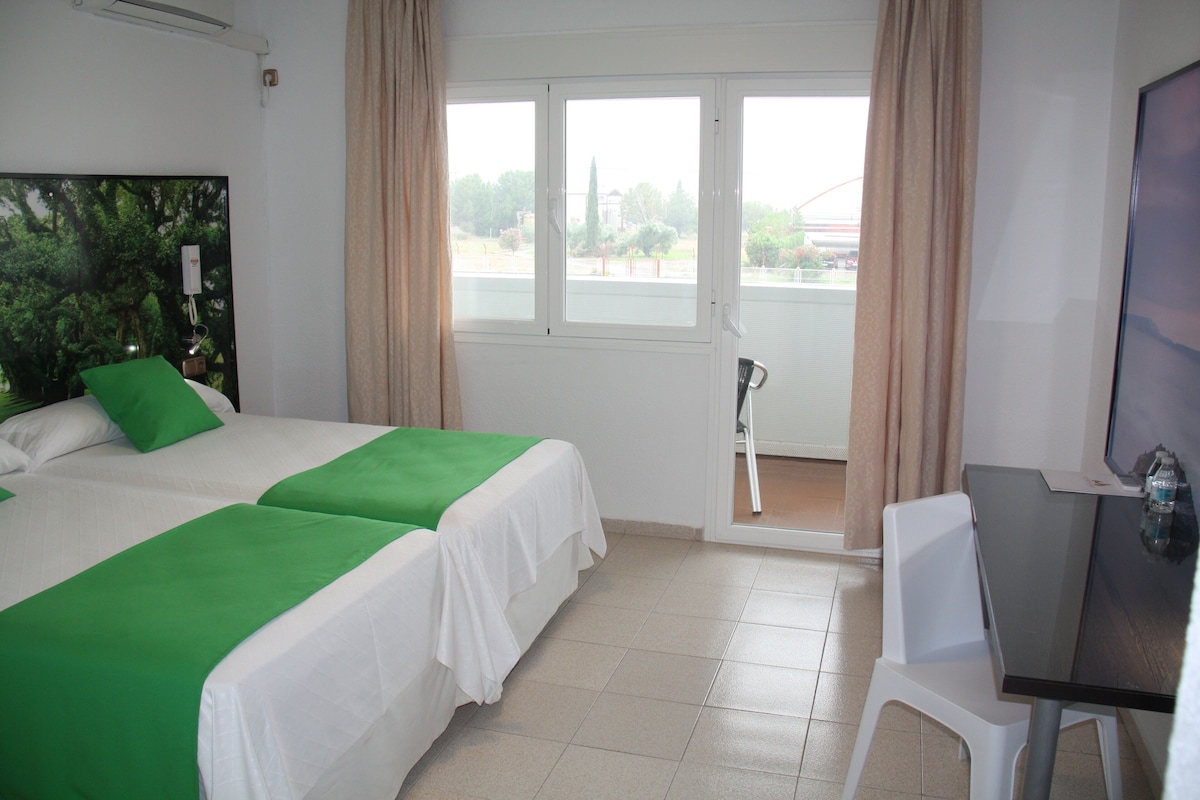 A hotel room with two beds, a desk, and a balcony.