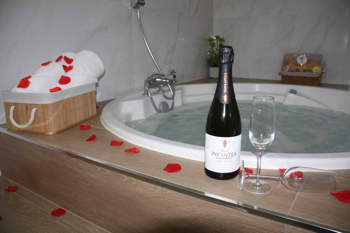 Una bañera con pétalos de rosa, una botella de vino Infantes Brut Reserva y una copa de vino.