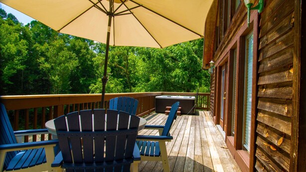 Um deck de madeira com cadeiras Adirondack e um grande guarda-sol, com vista para uma área arborizada.
