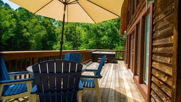 A wooden deck with Adirondack chairs and a large umbrella, overlooking a forested area.