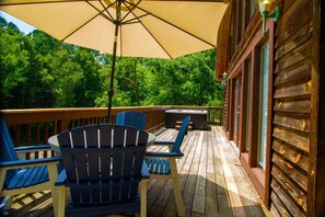 A wooden deck with Adirondack chairs and a large umbrella, overlooking a forested area. - Smoky Waters by Hosteeva (Sevierville)