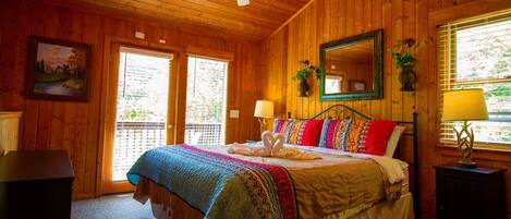Un dormitorio de cabaña de madera con una cama, dos lámparas de noche, un ventilador de techo y una ventana con persianas.