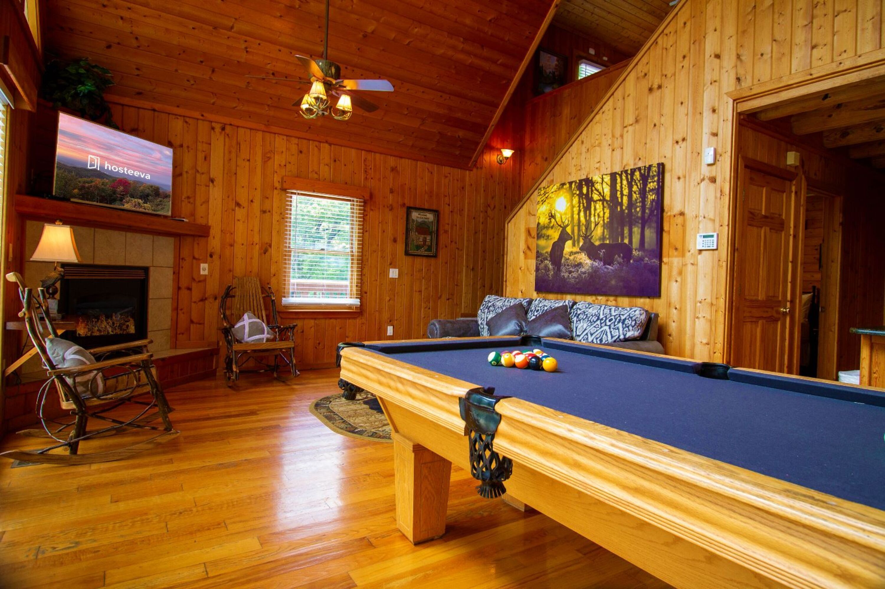 Interno di una baita in legno con tavolo da biliardo, camino, televisore e un quadro appeso al muro.