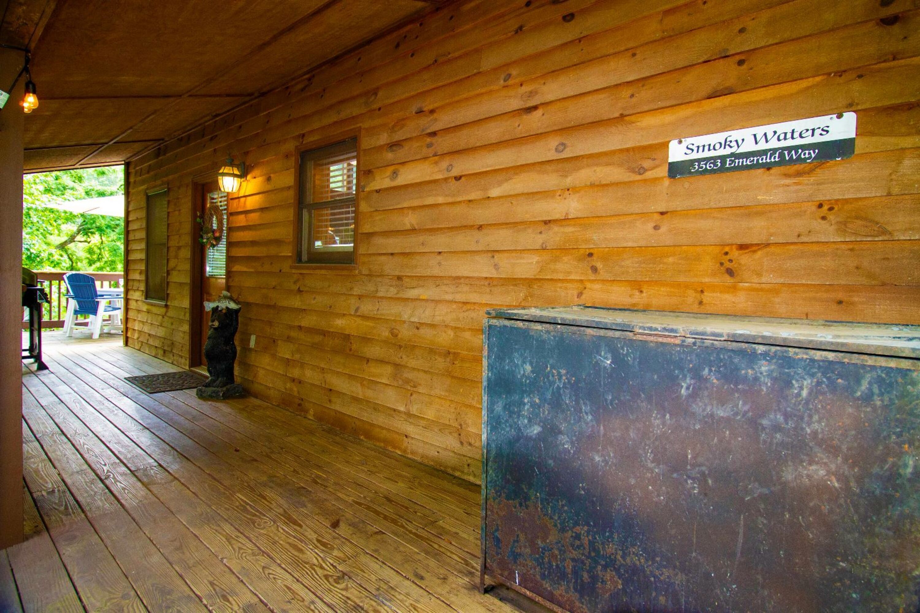 A wooden cabin with a porch, a sign reading "Smoky Waters 3563 Emerald Way", and a rustic metal box.