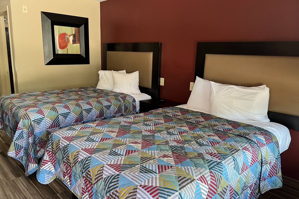 A hotel room with two beds, each with a colorful geometric-patterned bedspread and white pillows.