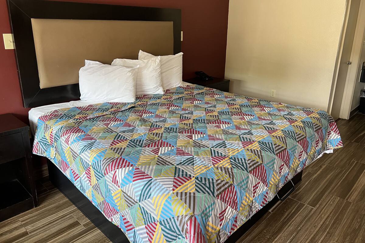 A hotel room with a bed, a headboard, a nightstand, and a wooden floor.
