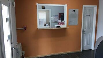A room with an orange wall, a white door, a white-framed mirror, and a small shelf with items.