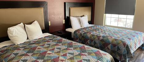 Habitación de hotel con dos camas, cada una con una colcha estampada y almohadas blancas. Se ve una ventana con vistas al exterior.