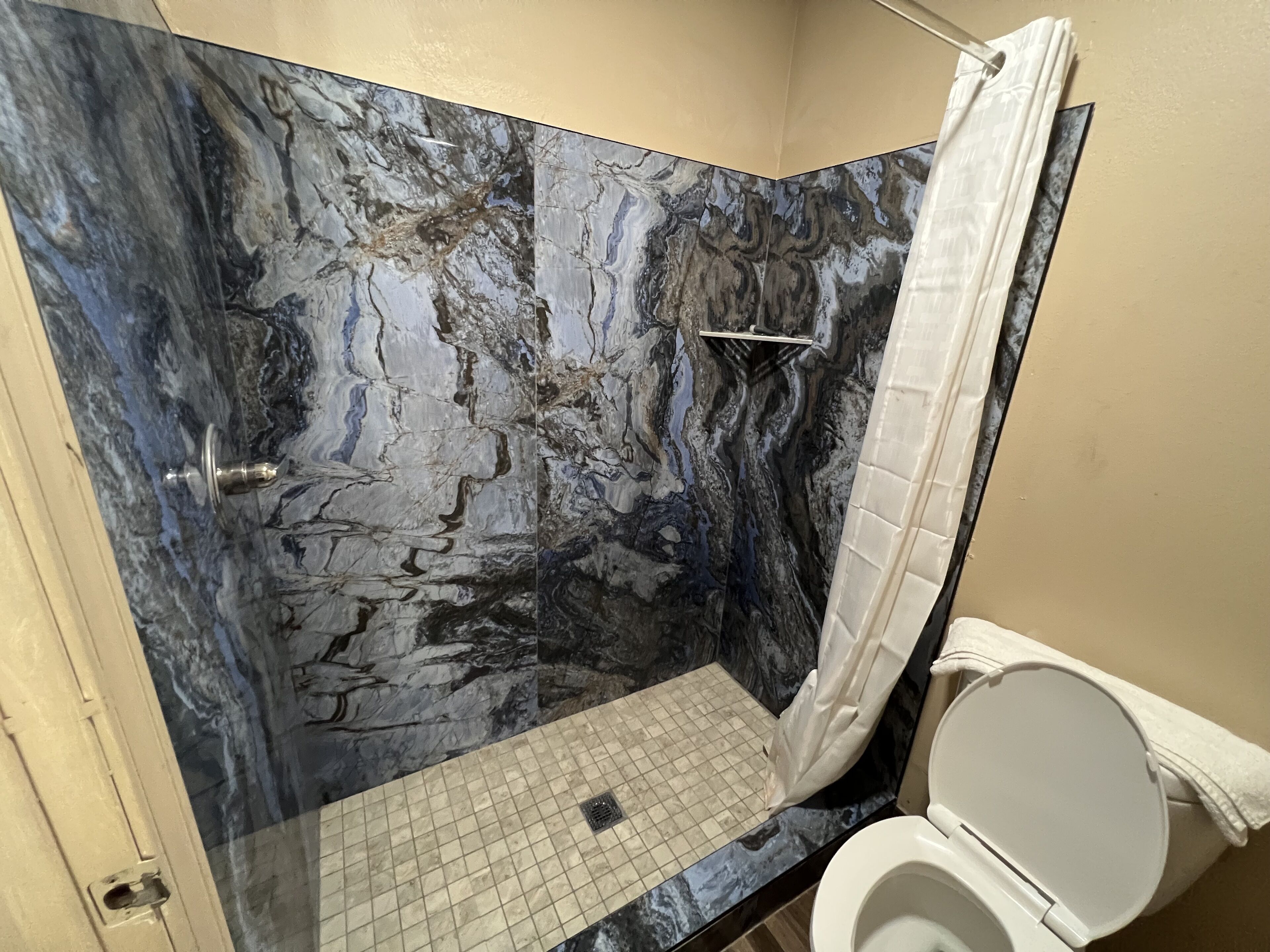 A bathroom with a marble wall, a shower, and a toilet.