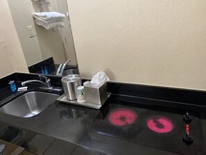 A bathroom with a sink, mirror, towel rack, and a stove with red lights. - Cajun Country Inn (Gonzales)
