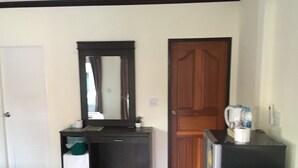 A hotel room with a wooden door, a small desk with a mirror, a coffee machine, and a trash bin. - Sai Kaew House (Mai Khao)
