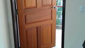 A wooden door with a simple design, a tiled floor, and a visible electrical outlet on the wall. - Sai Kaew House (Mai Khao)