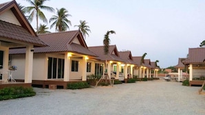A row of bungalow-style hotel rooms with tiled roofs, a gravel driveway, and palm trees in the background. - Sai Kaew House (Mai Khao)