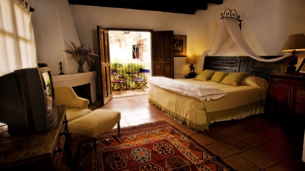 A bedroom with a bed, a chair, a television, and a fireplace. - Casa Capuchinas (Antigua Guatemala)