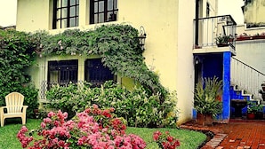 A building with a white exterior, a brick pathway, and a chair in the foreground. - Casa Capuchinas (Antigua Guatemala)