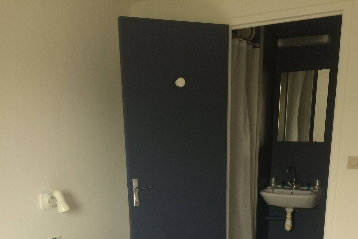 A hotel room with a bed, a door, a bathroom with a sink, and a mirror.