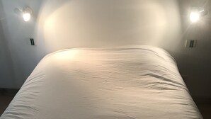 A bed with a white sheet and a folded towel, two wall-mounted lights, and a white wall. - Le Salin (Brehal)